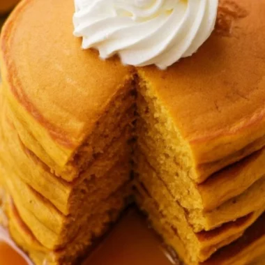 Fluffy pumpkin pancakes stacked on a plate with maple syrup