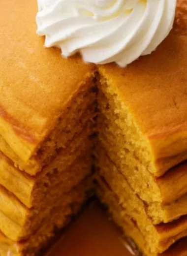 Fluffy pumpkin pancakes stacked on a plate with maple syrup