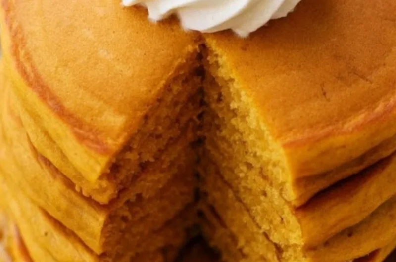 Fluffy pumpkin pancakes stacked on a plate with maple syrup